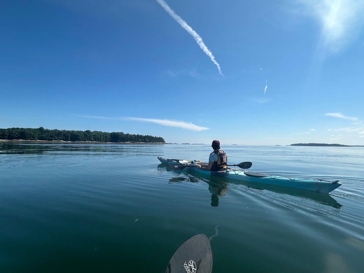 Solo sea kayaker on a calm bay, under a blue sky.
