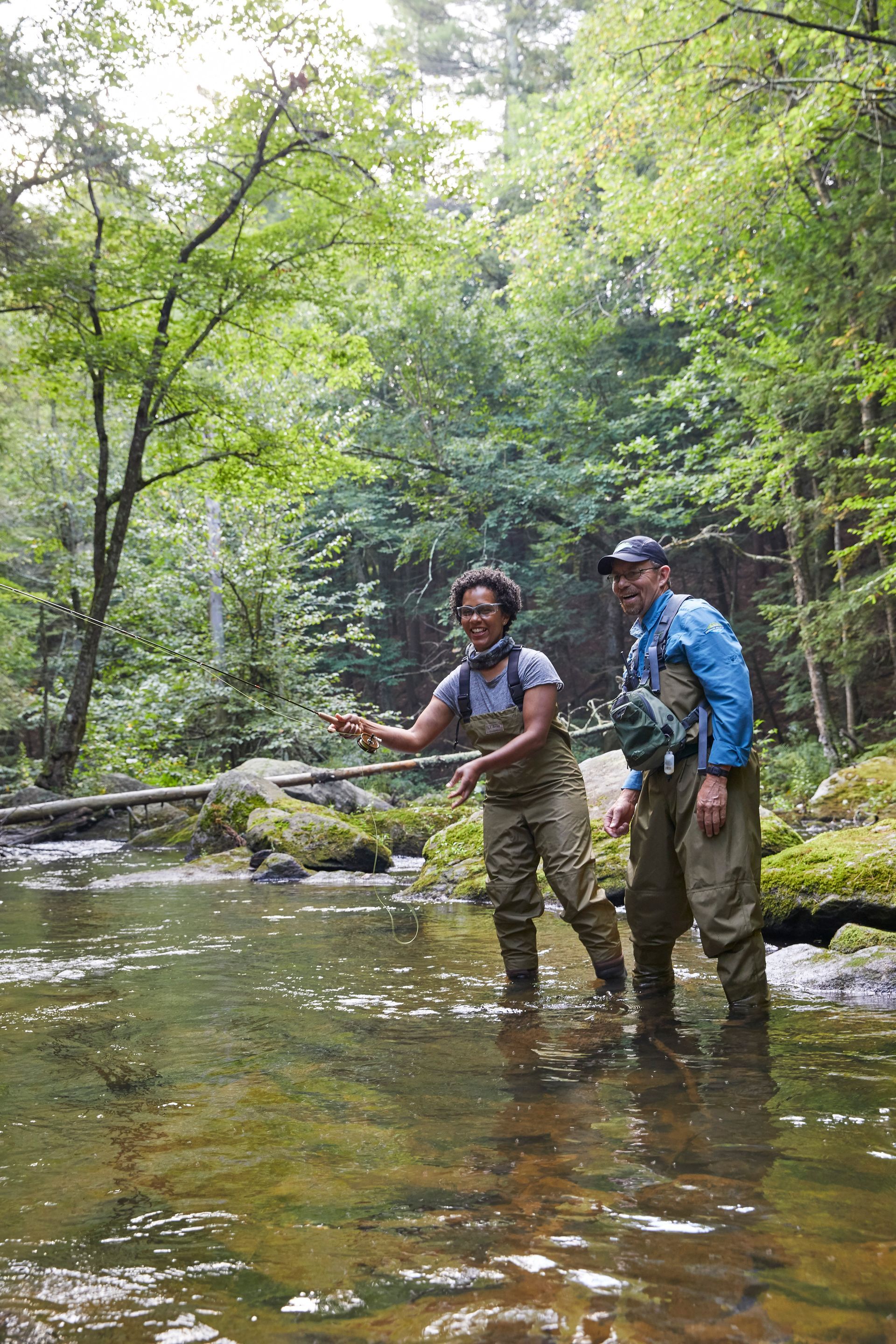 Woman fly fishing in a stream with a guide looking on.