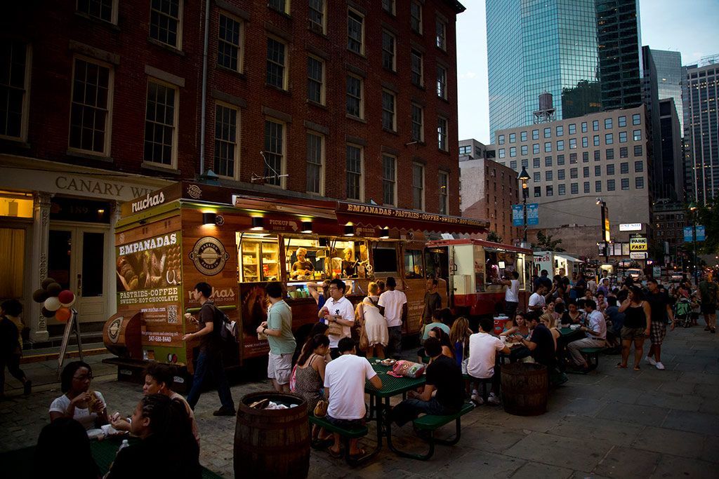 A group of people are sitting at picnic tables in front of a food truck.