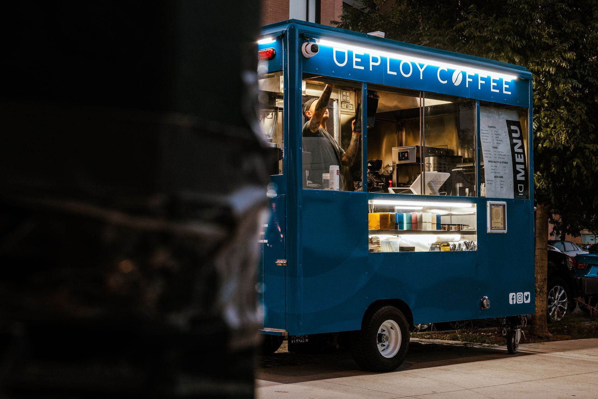 A blue food truck called deploy coffee is parked on the side of the road.