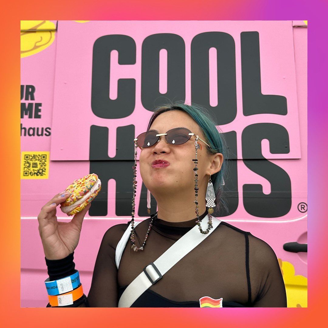 A woman is eating a donut in front of a pink van that says cool haus
