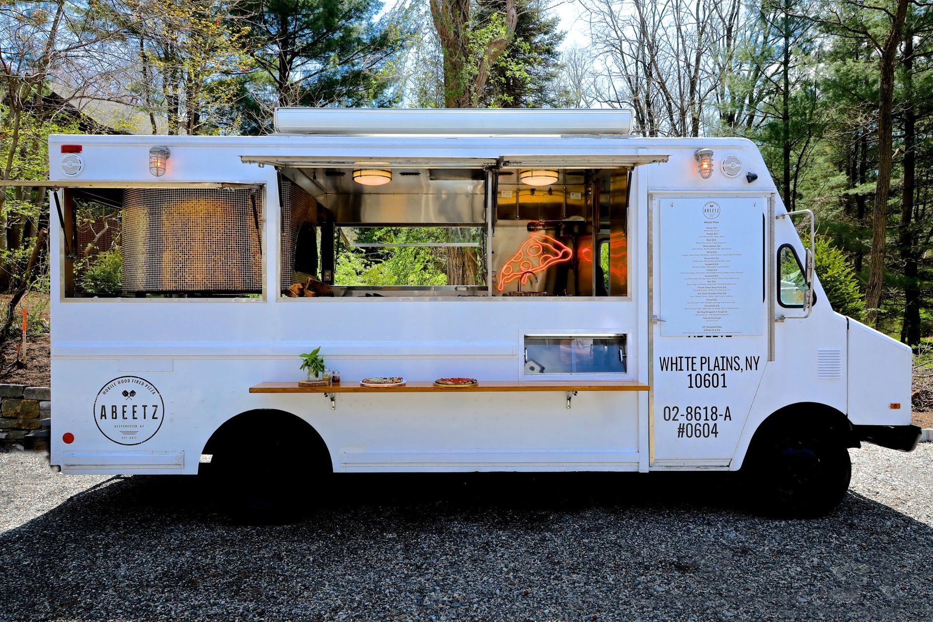A white food truck is parked in a gravel lot.