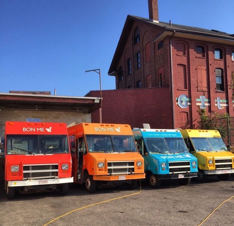 A row of food trucks are parked in front of a building that says bon me