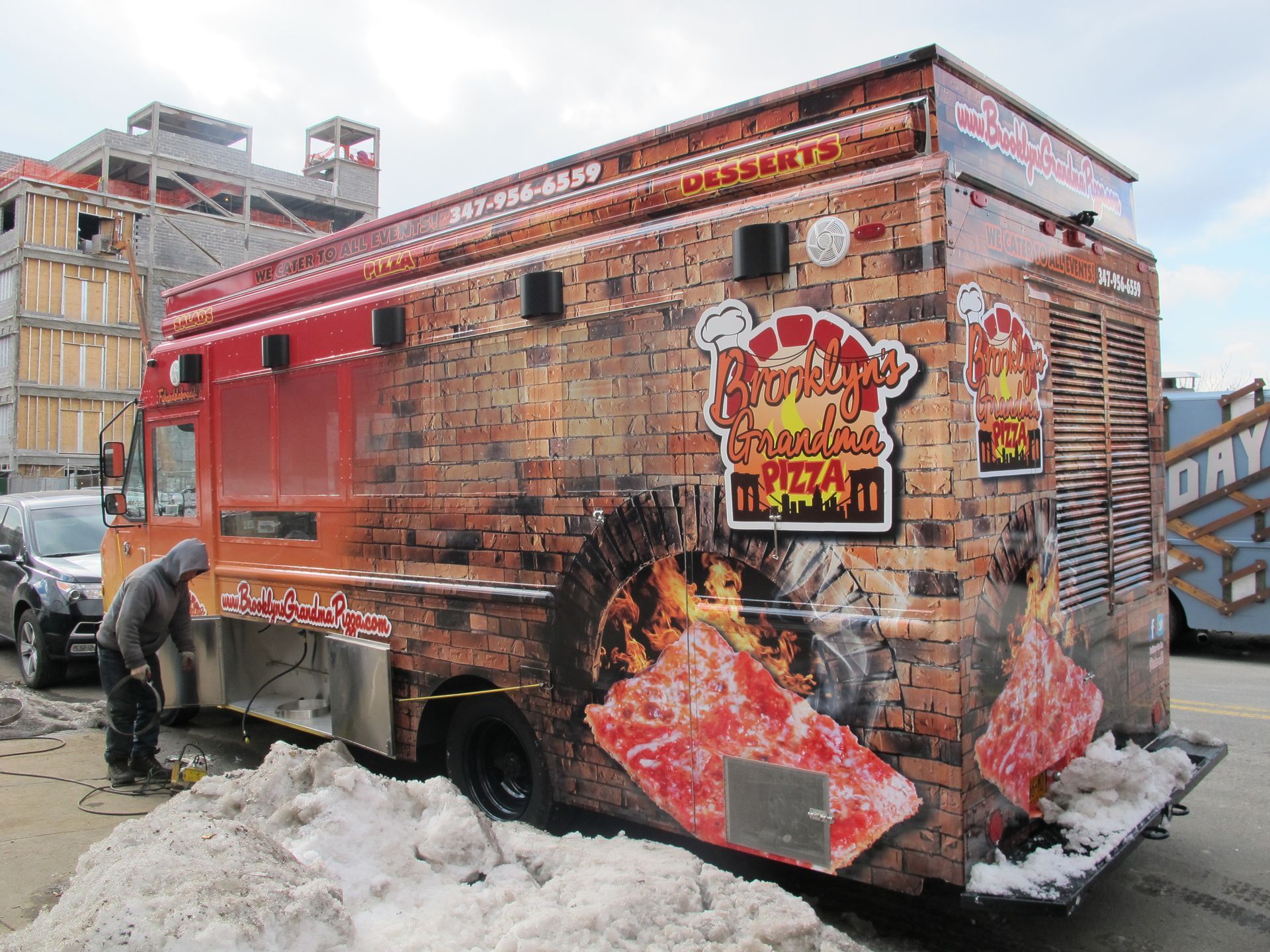A man is working on a food truck with a pizza on the side.