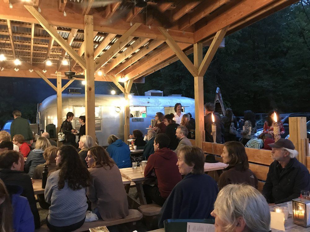 A group of people are sitting at tables under a covered area.