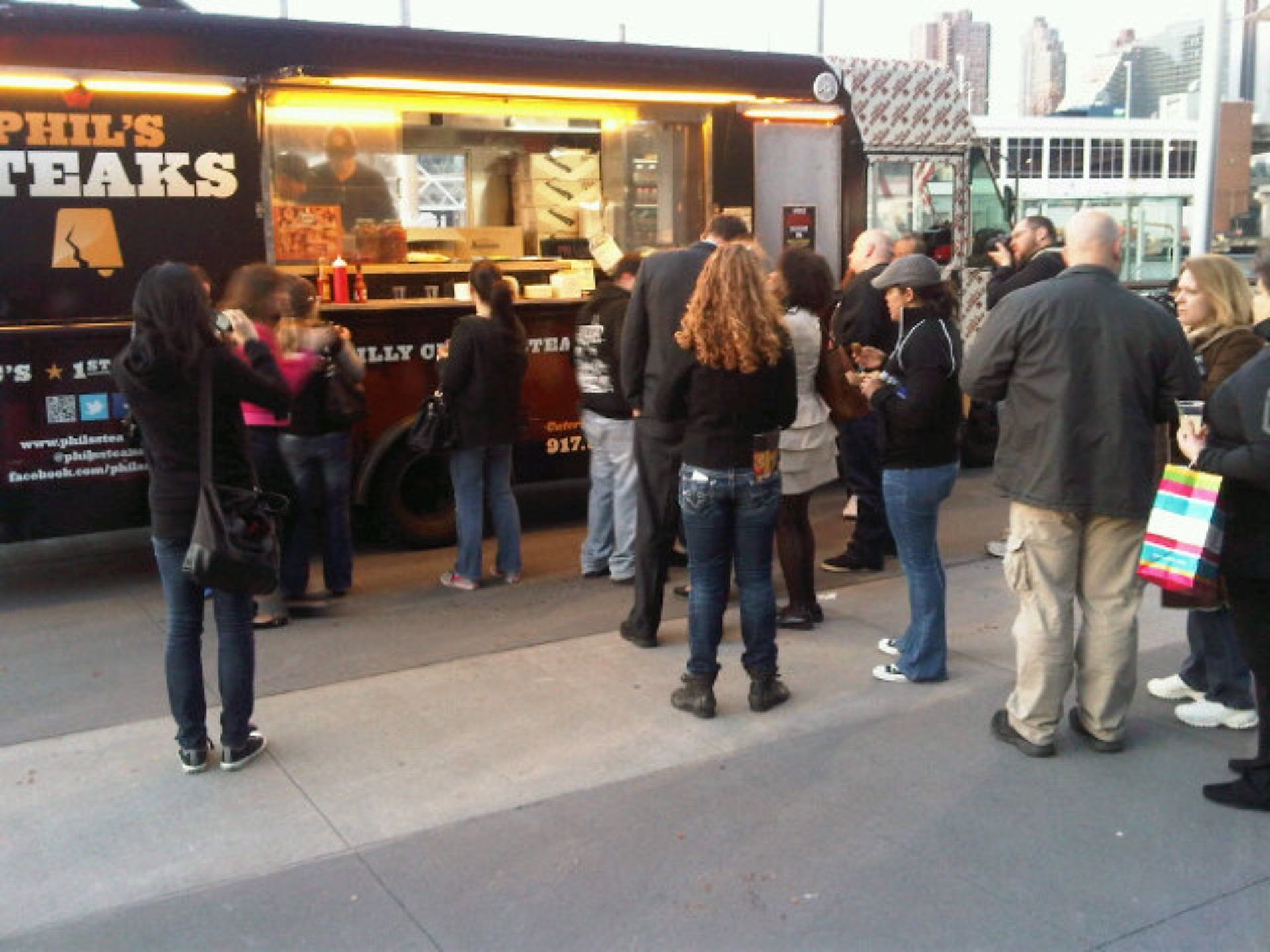 A group of people standing in front of a phil 's steaks food truck