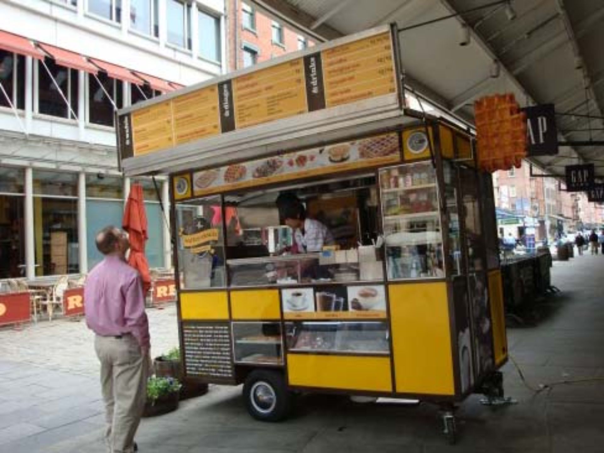 A man standing in front of a food cart that says gap on it