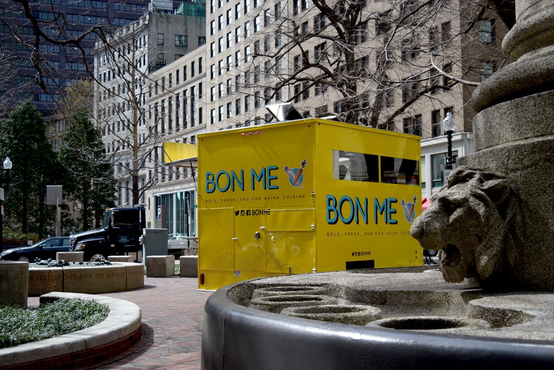 A yellow bon me food truck is parked in front of a building