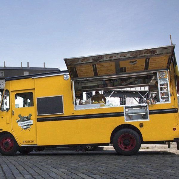 A yellow food truck is parked on a cobblestone street