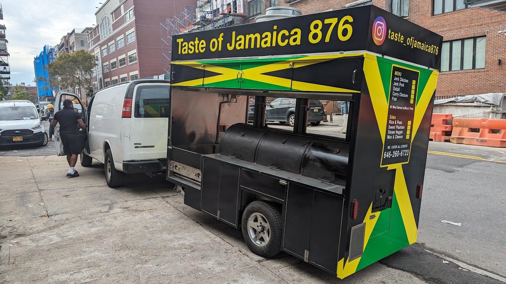 A food truck is parked on the side of the road next to a white van.