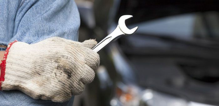 A mechanic is holding a wrench in his hands in front of a car.