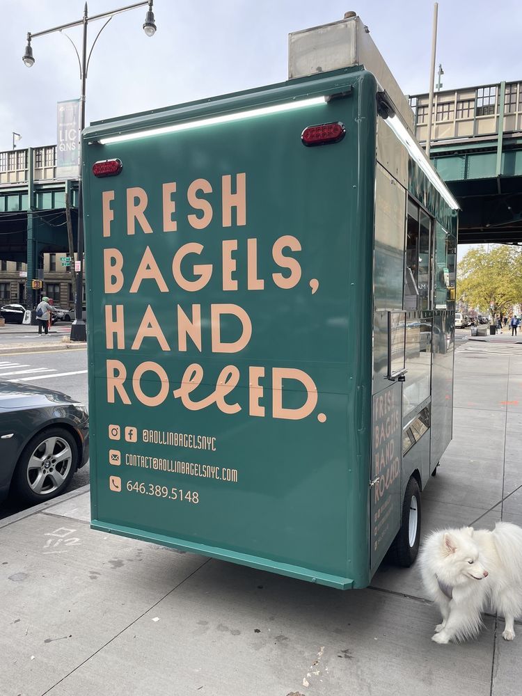 A green food truck that says fresh bagels hand rolled
