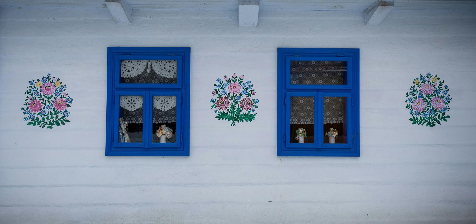 A white house with blue windows and flowers painted on the wall.