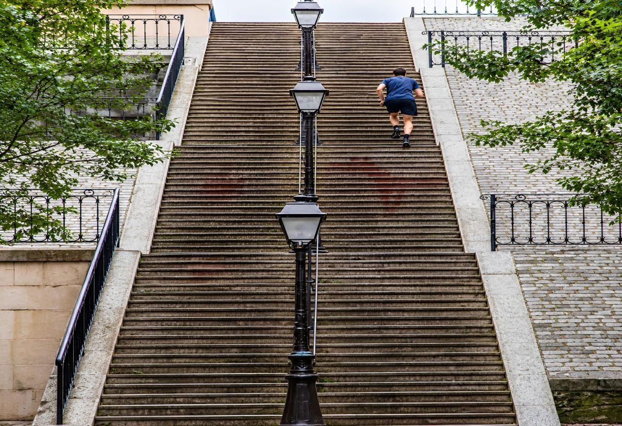 Steep outdoor stairway with a central lamp post; one person in a blue jacket climbs near the top.