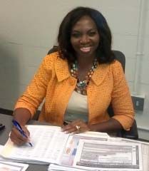 Woman in an orange blazer smiling while signing documents at a desk.