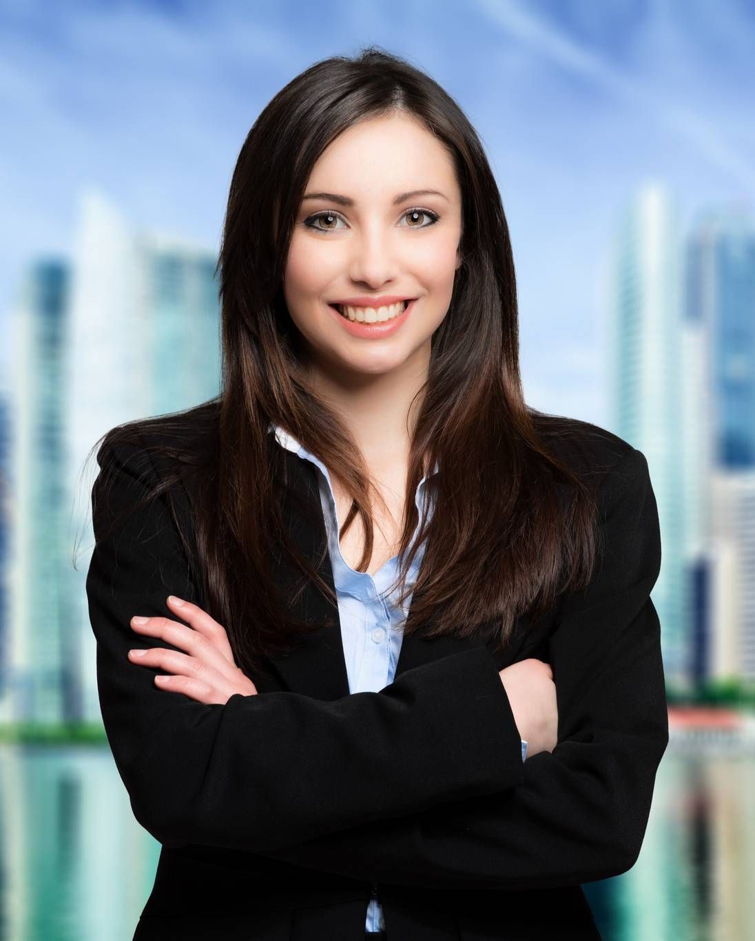 Smiling professional in a black blazer, arms crossed, standing before a blurred city skyline.
