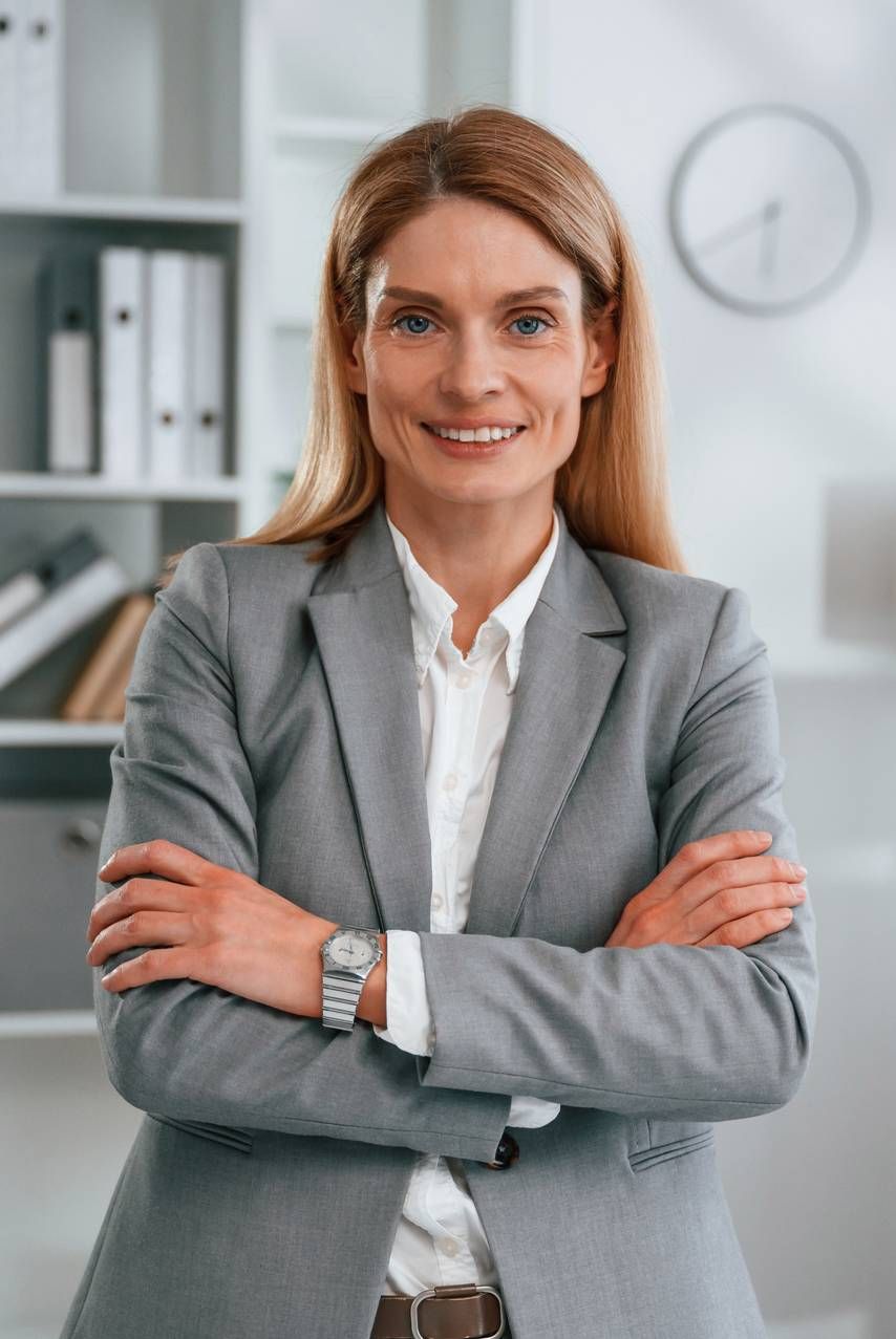 Smiling professional in gray blazer with arms crossed in an office