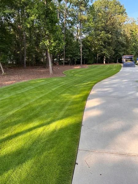 Curved green lawn beside a paved path with trees and a golf cart in the distance