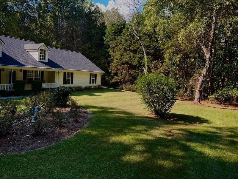 Yellow house with a screened porch beside a green lawn and trees in a sunny yard