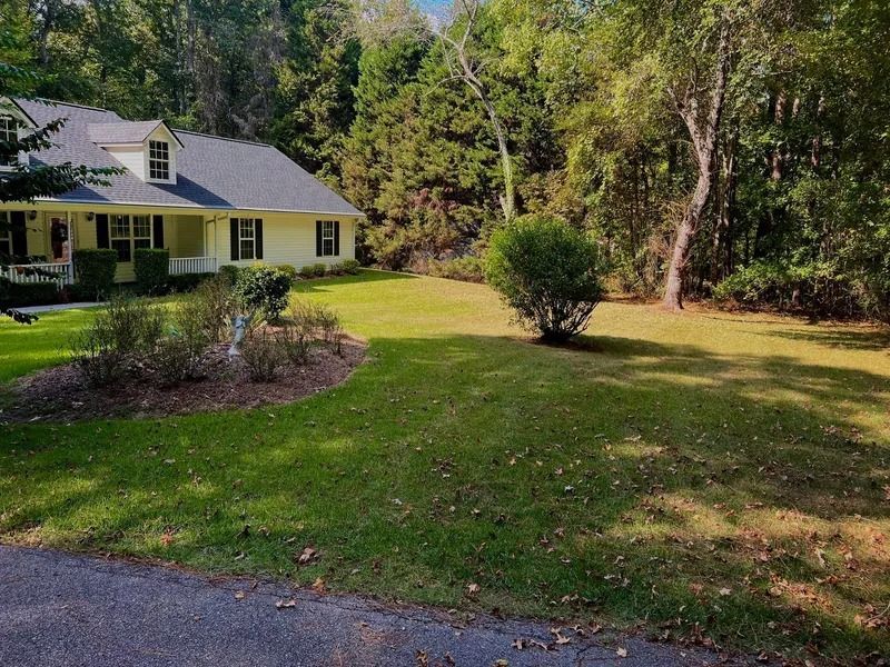 Yellow house with green lawn, driveway, and trees in a wooded yard