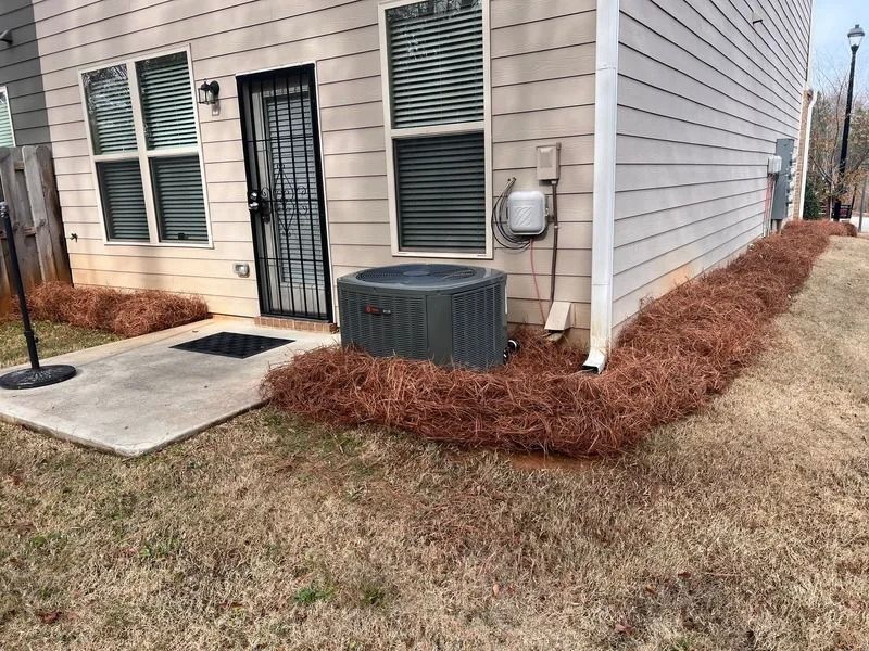 Exterior corner of a house with windows, a door, air conditioner unit, and mulch bed along the foundation