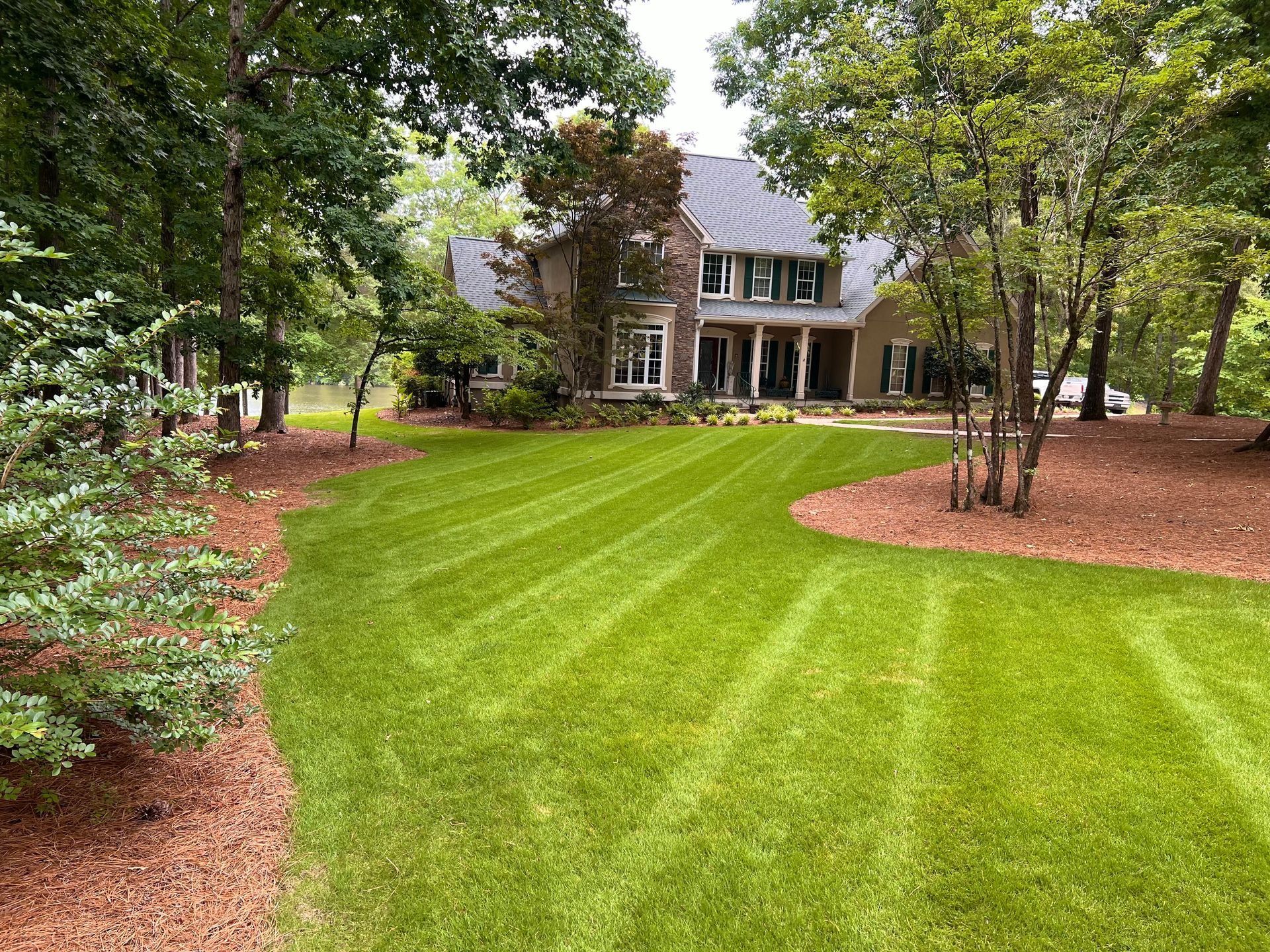 Large house with a manicured green lawn and trees in a landscaped yard