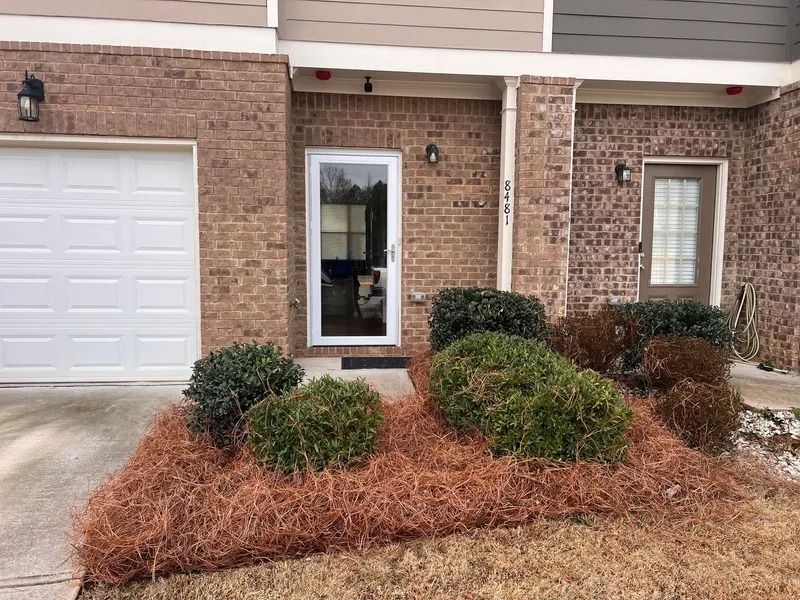 Front of a brick townhouse with garage, windows, and shrubs in winter landscaping