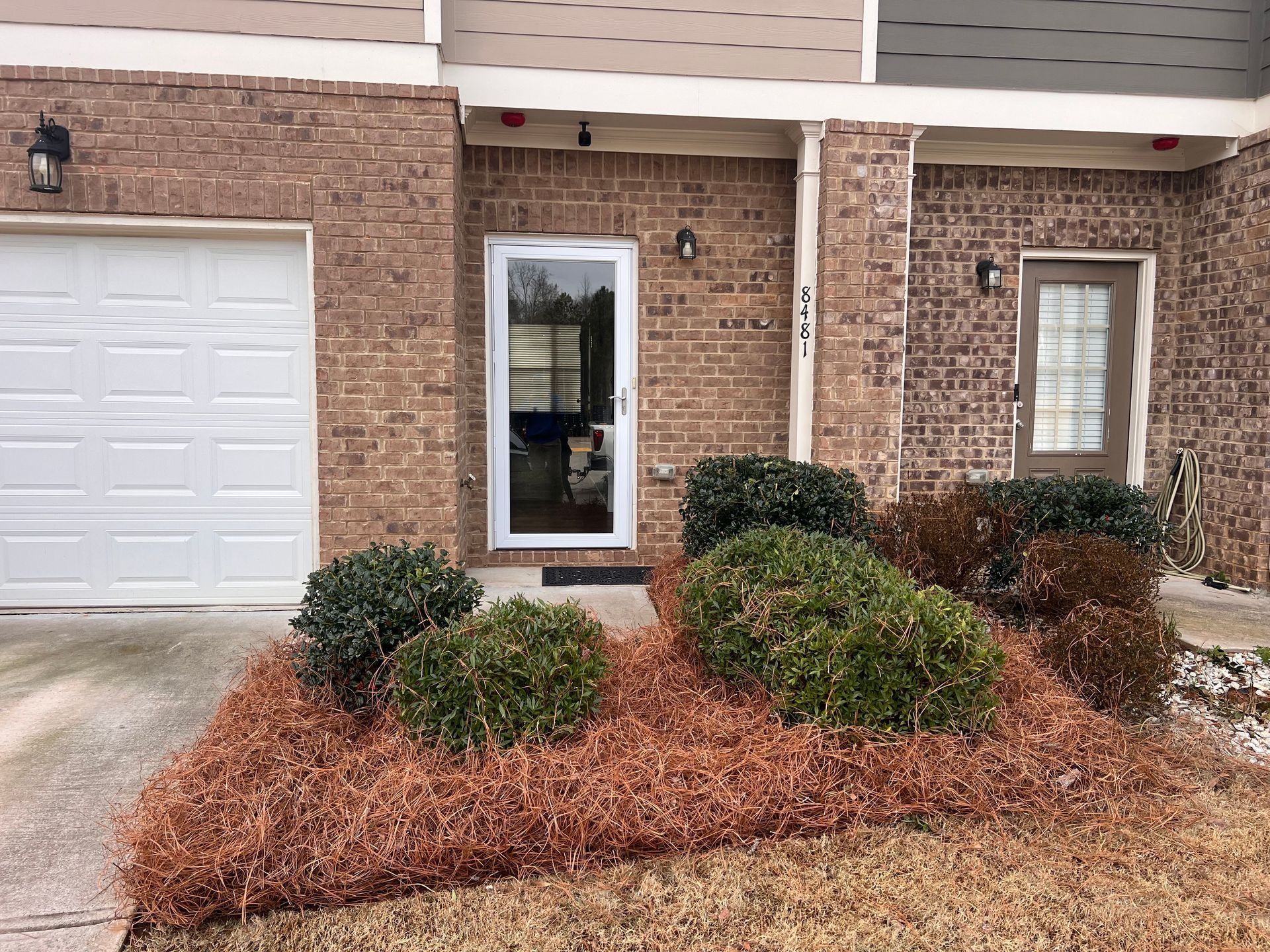 Suburban townhouse exterior with brick facade, garage, front door, and landscaped shrubs in front yard