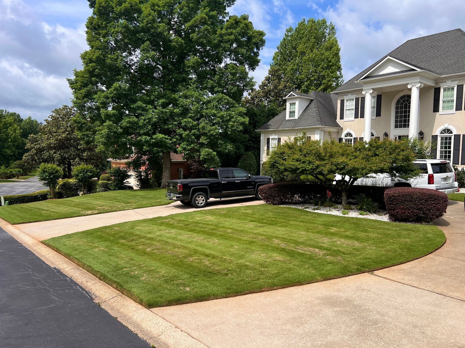Suburban house with a black truck parked on a driveway beside a neatly mowed lawn and trees