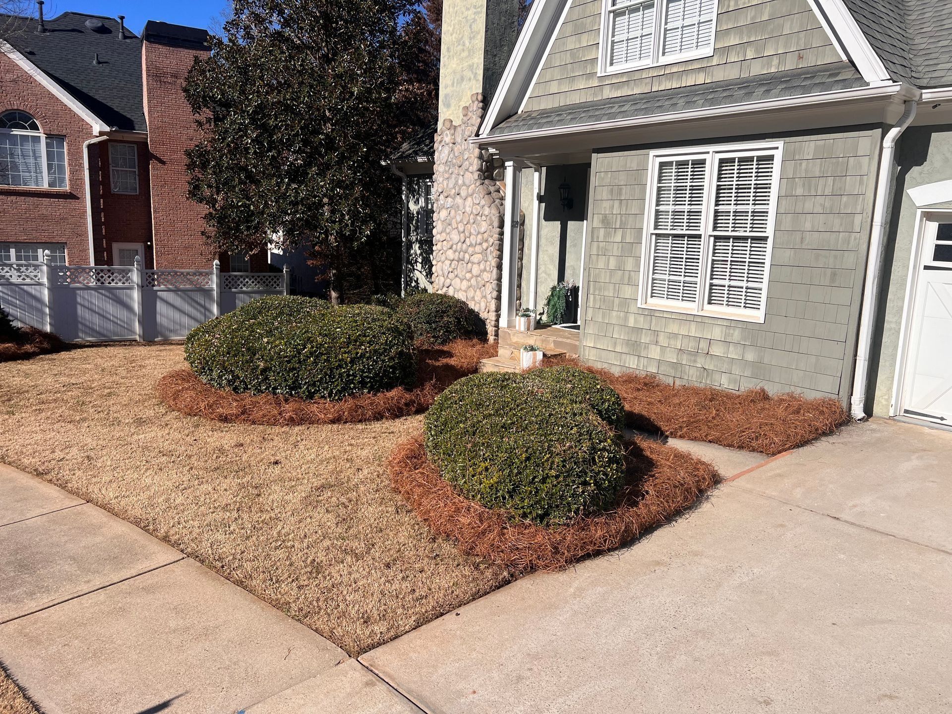 Suburban house front yard with trimmed shrubs, mulch beds, and a concrete driveway