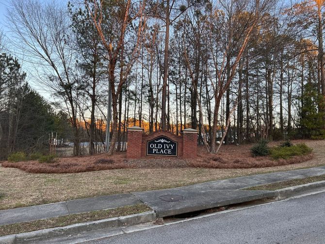 Stone entrance sign beside a road, framed by leafless trees and landscaping at dusk.