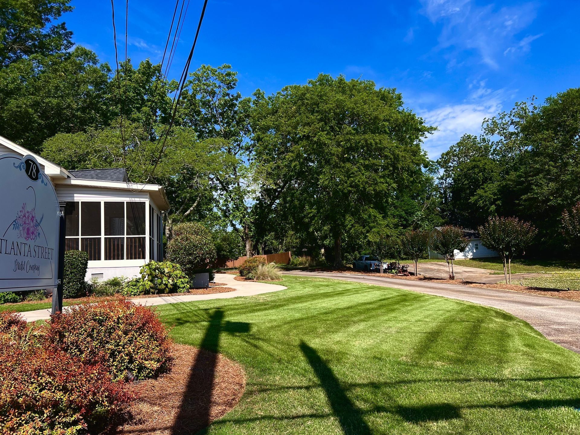 Sunny backyard with neatly mowed lawn, trees, and a house patio under a blue sky