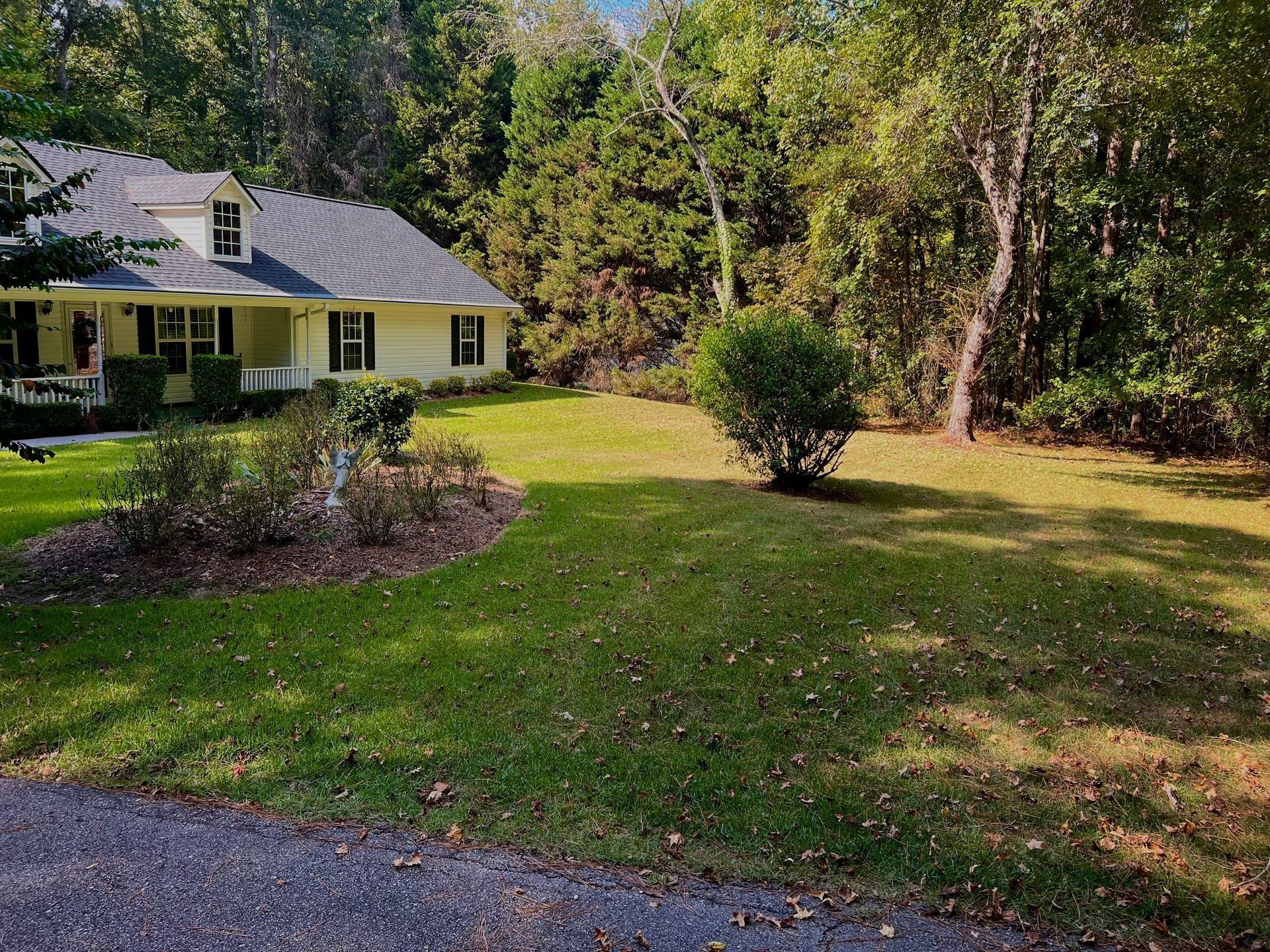 Person raking soil in a yard near a brick house and green bushes