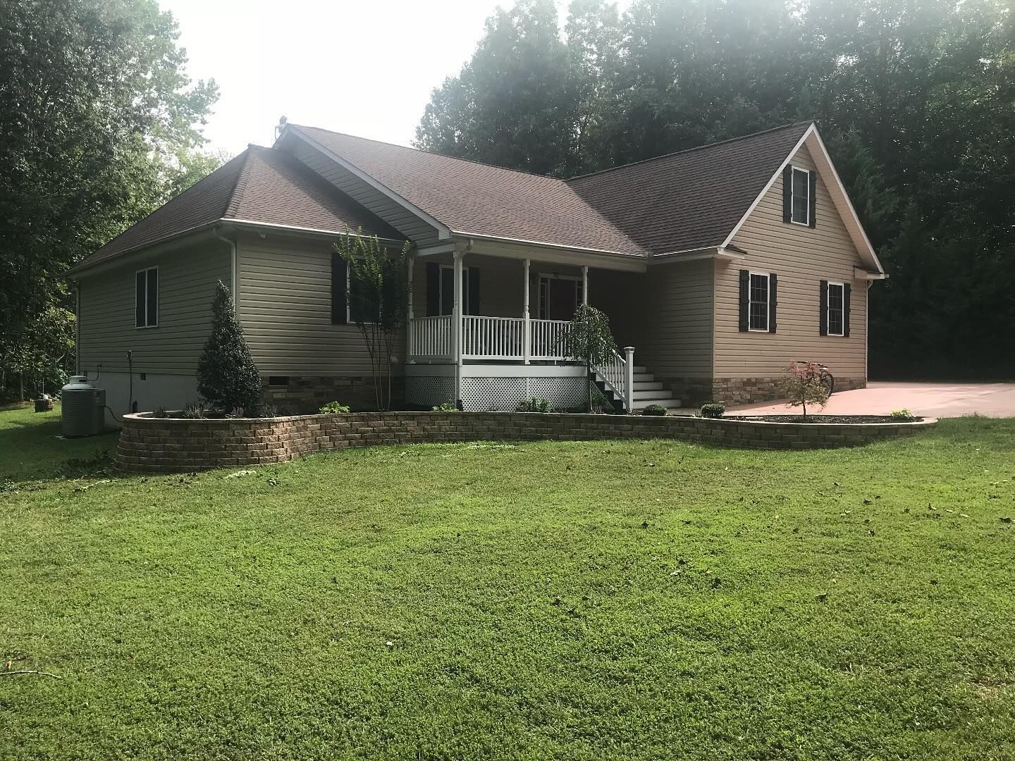 Single-story beige house with a brown roof, front porch, and a large green lawn.