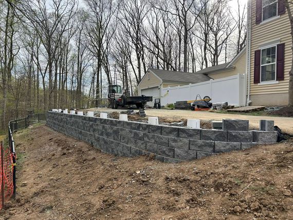 Retaining wall under construction beside a beige house on a wooded hillside