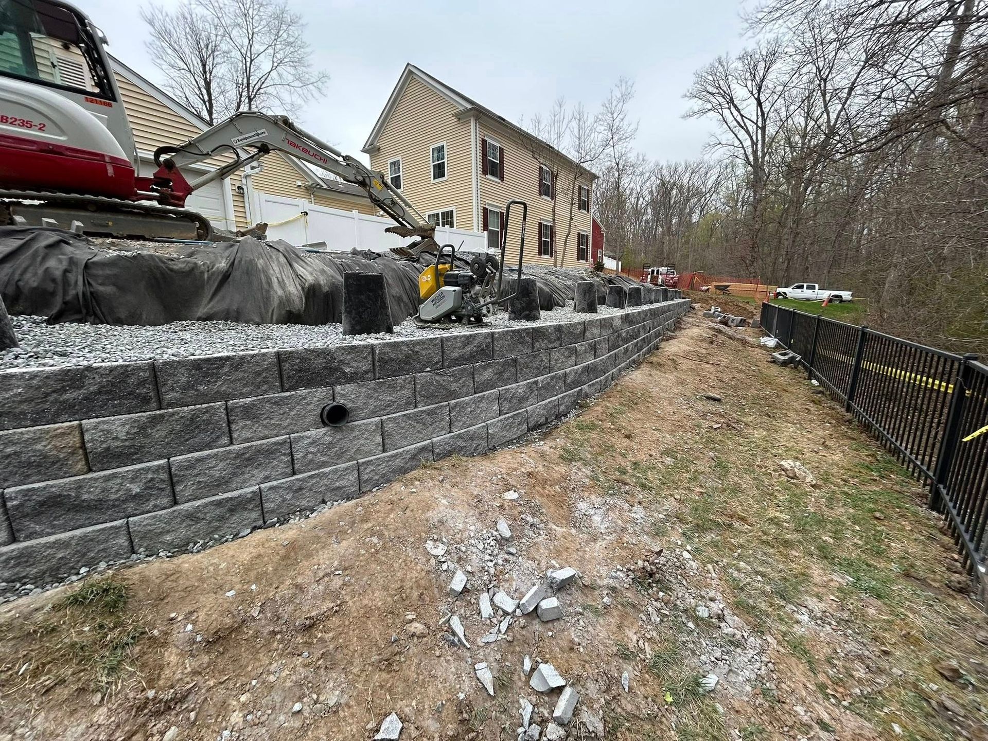 Construction site with stone retaining walls beside a yellow house on a muddy hillside