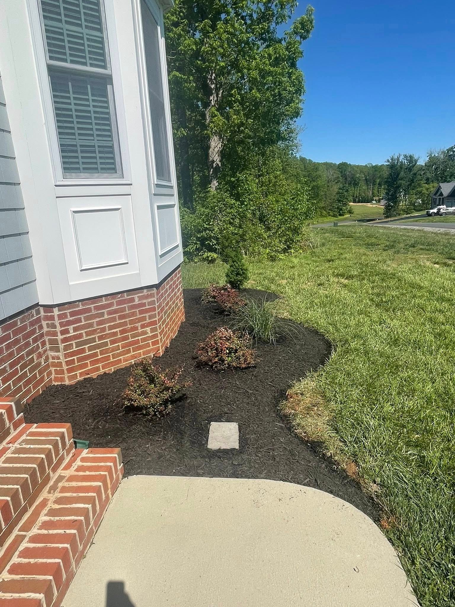 House corner with brick steps and a landscaped garden bed of mulch and shrubs next to a lawn