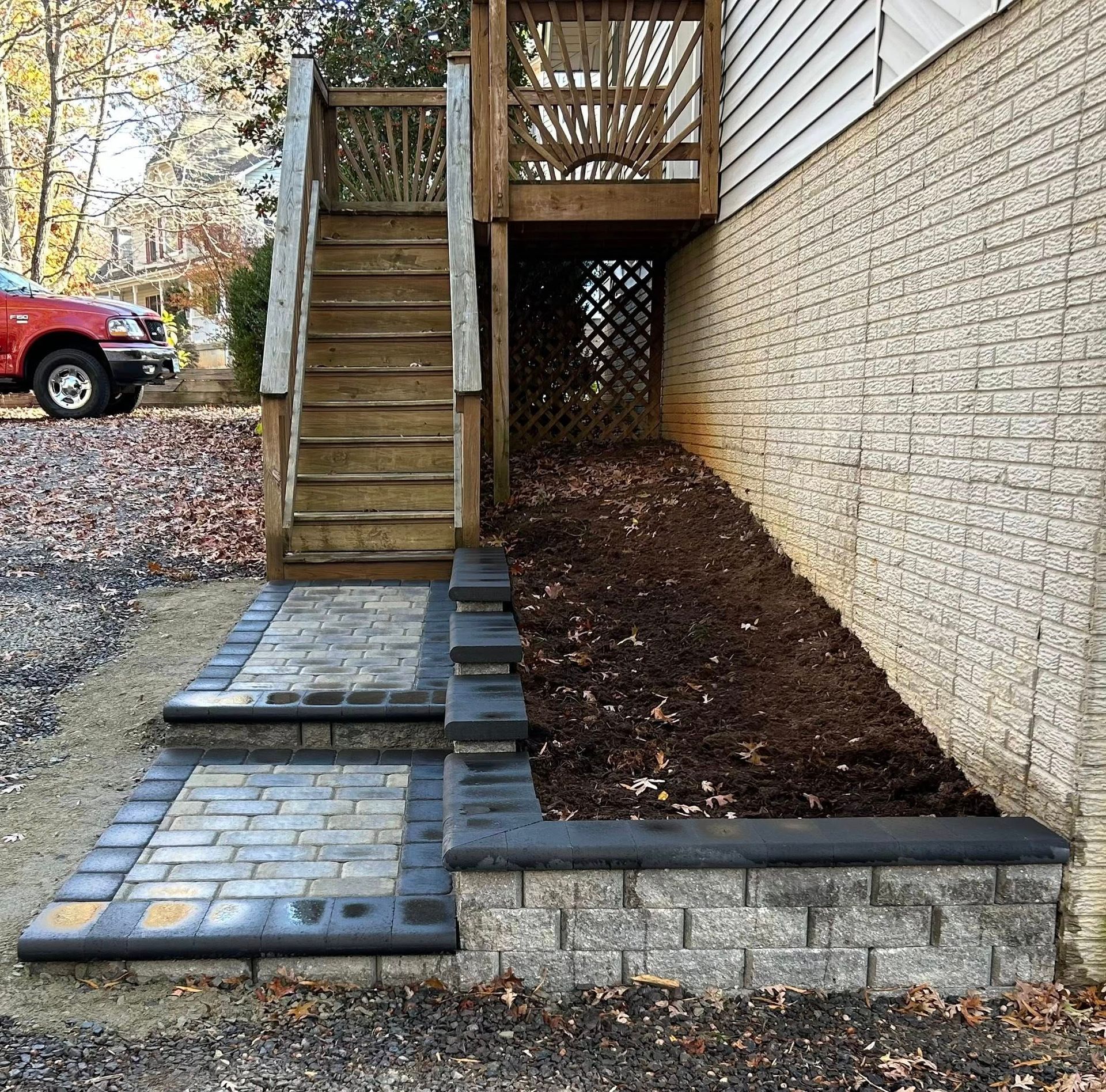 Side view of concrete steps and small paved walkway beside a brick house and autumn leaves.