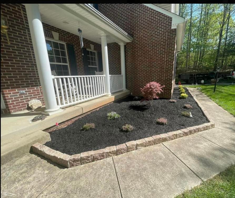 Brick house porch with white railing beside a mulched flower bed and concrete walkway