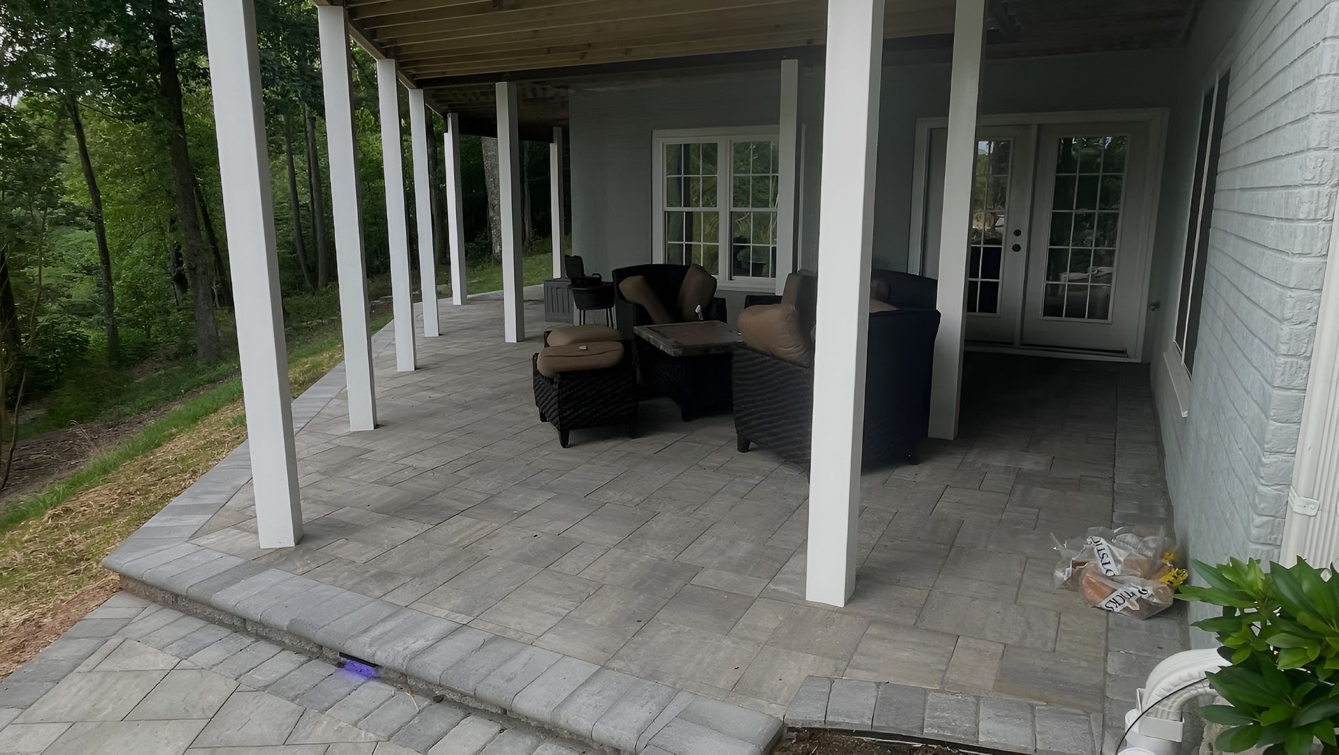 Covered patio with white columns, wicker seating, tiled floor, and doors leading indoors