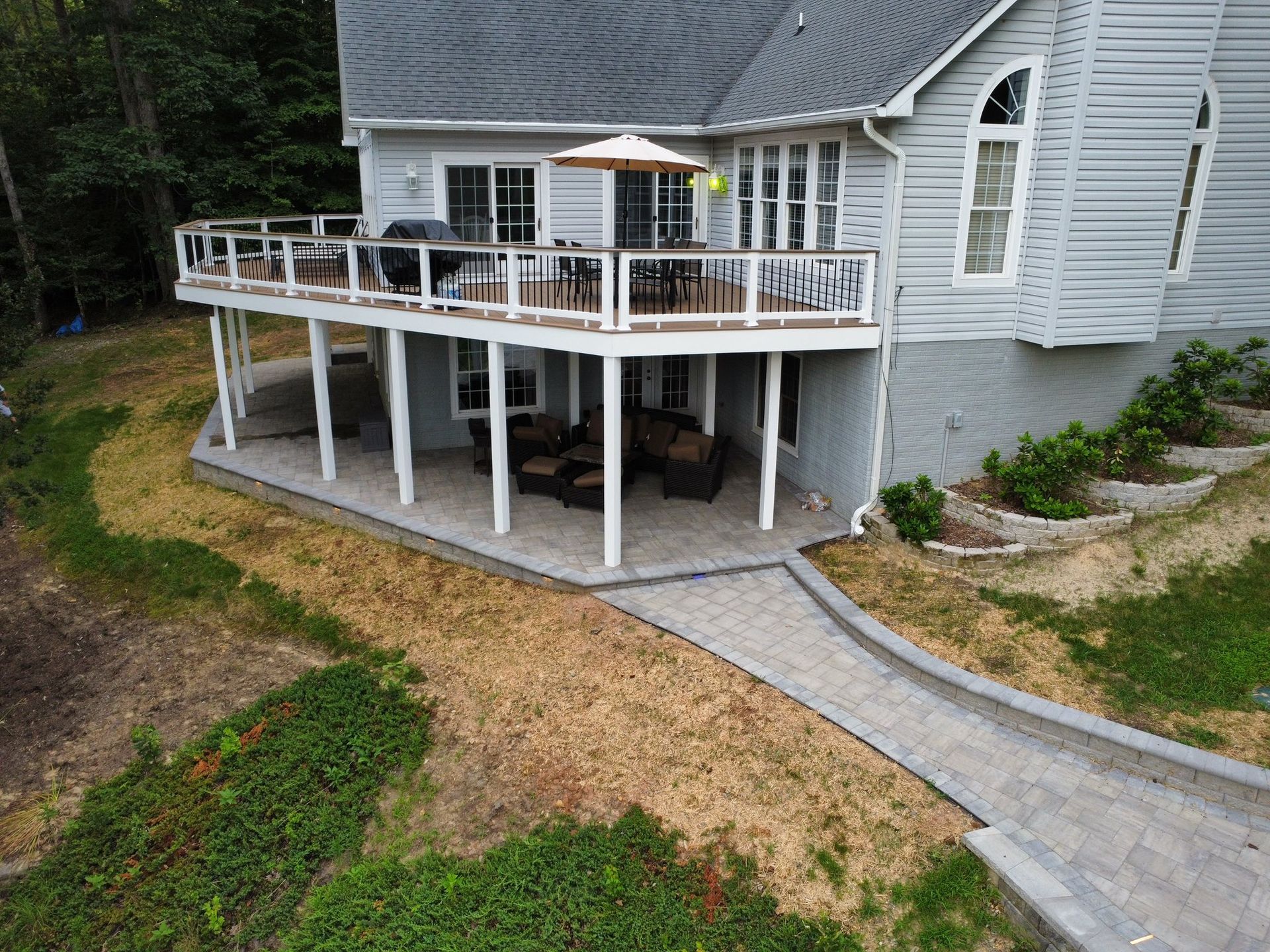 White house with a raised deck, stairs, and a curved paved walkway beside a sloped yard.