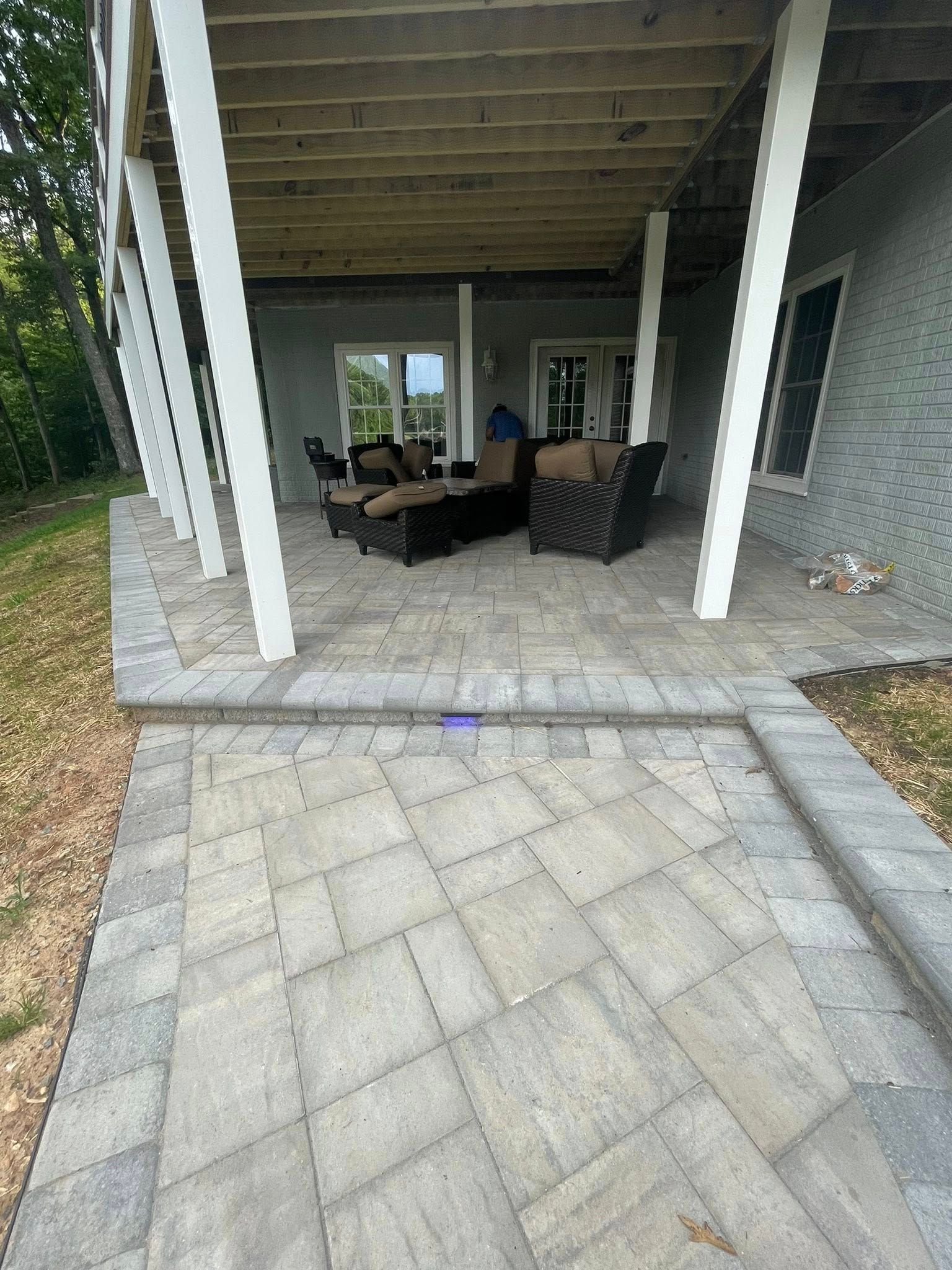 Covered patio with wicker seating and a paved paver patio in front of a house.