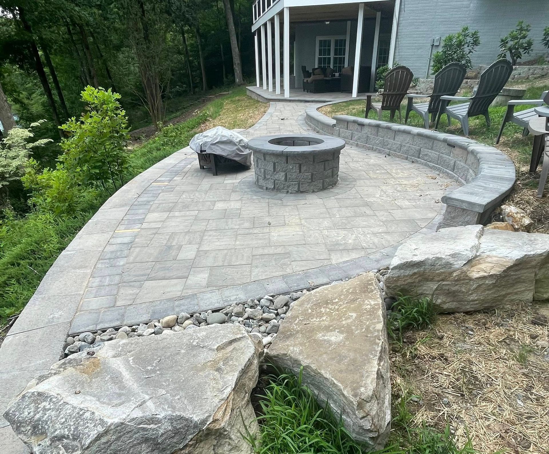 Stone patio with curved retaining wall, fire pit, and gazebo in a landscaped backyard