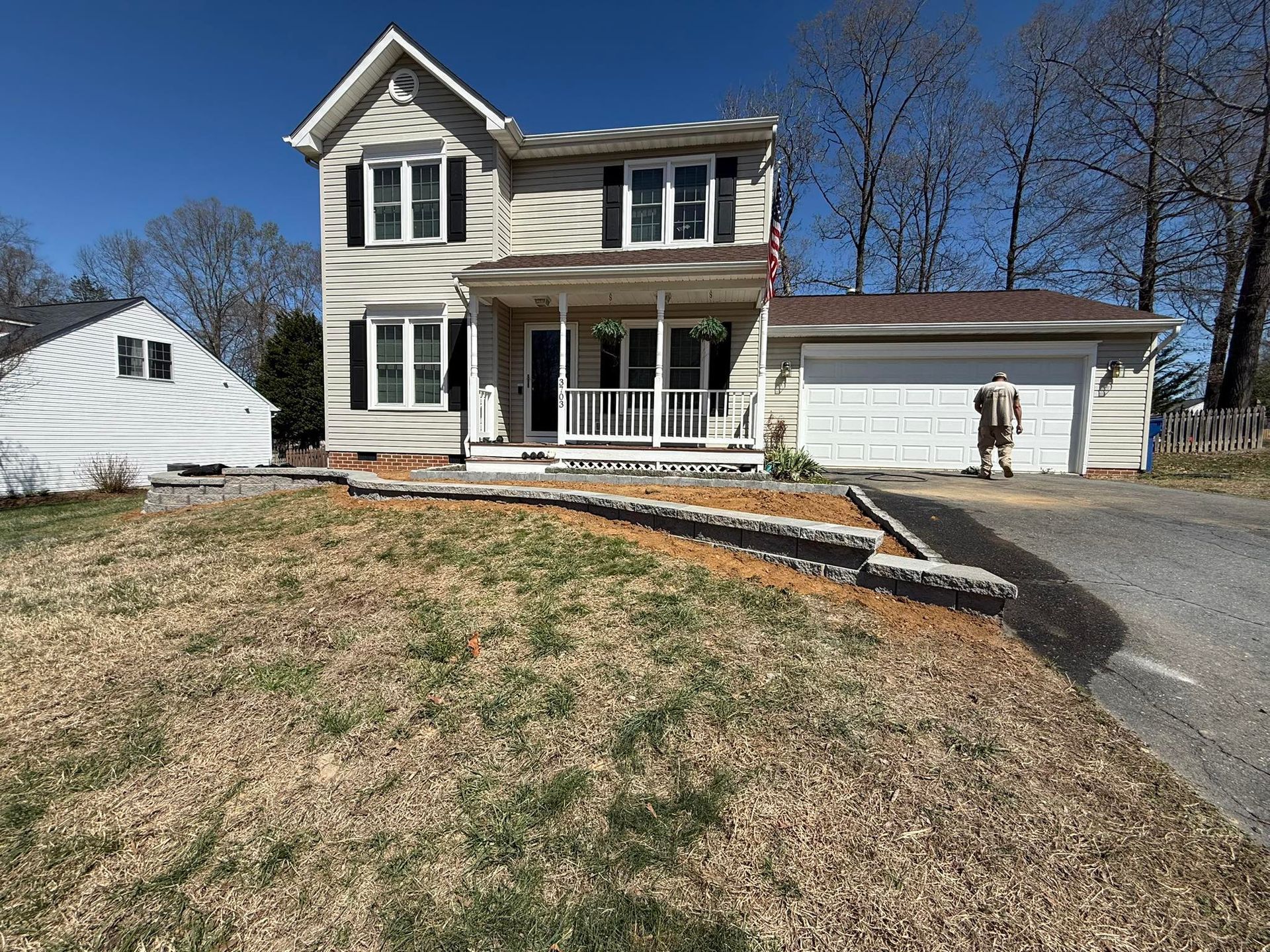 Two-story white house with front porch, detached garage, and sloped driveway on a sunny day