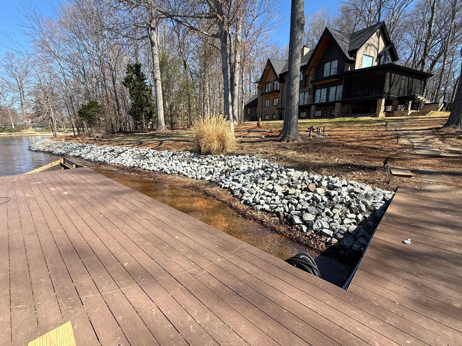 Wooden boardwalk beside a rocky shoreline, with a house and trees in the background.