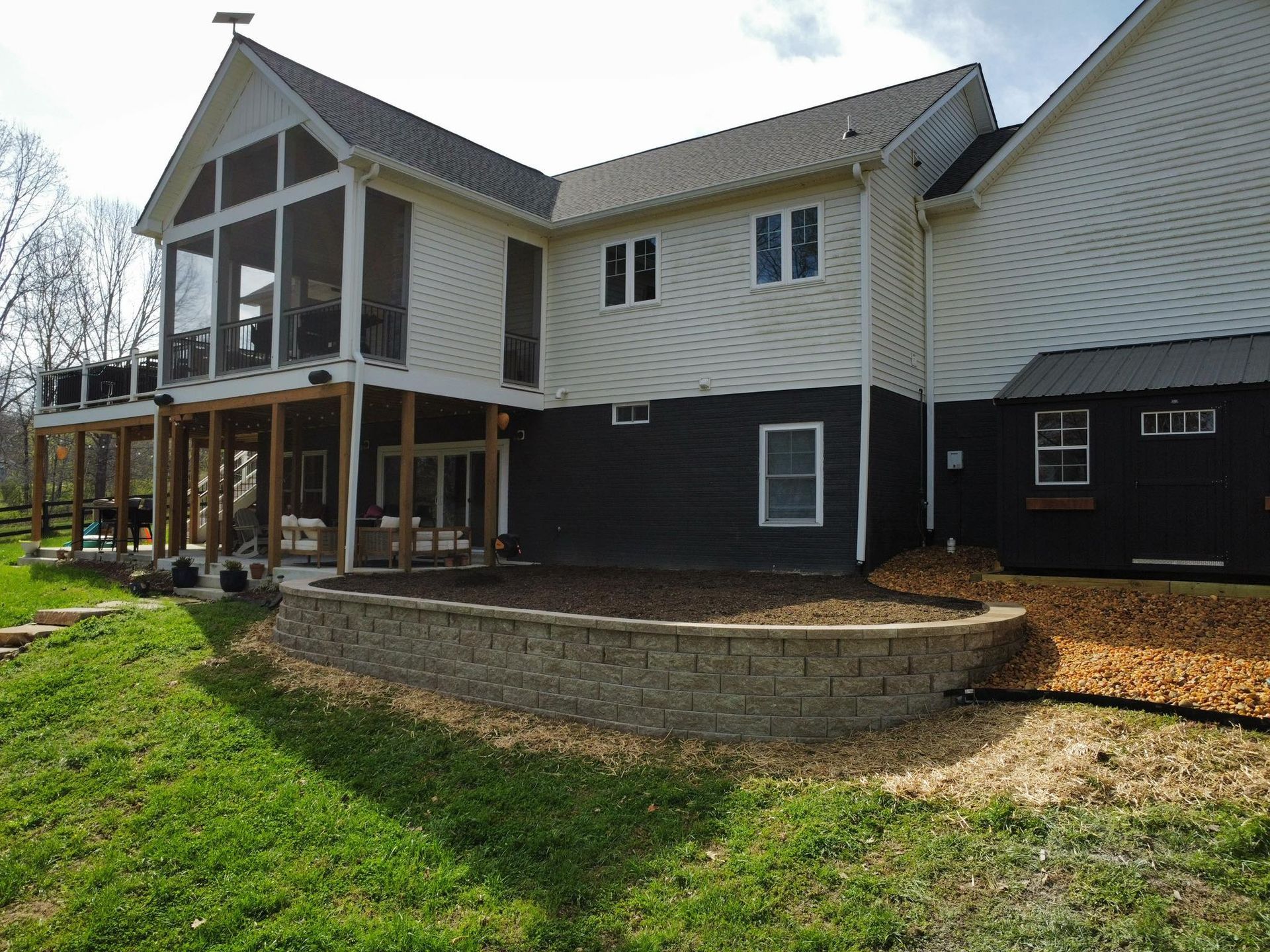 Two-story house with white siding, black lower level, and a raised porch on a grassy lot