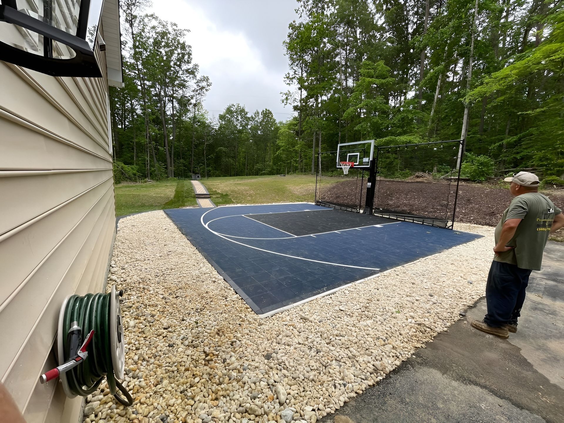 Outdoor driveway basketball court beside a house, with a man standing near the hoop.