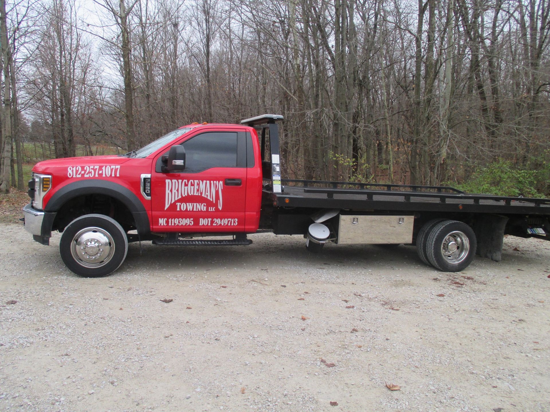 A red tow truck is parked in a gravel lot