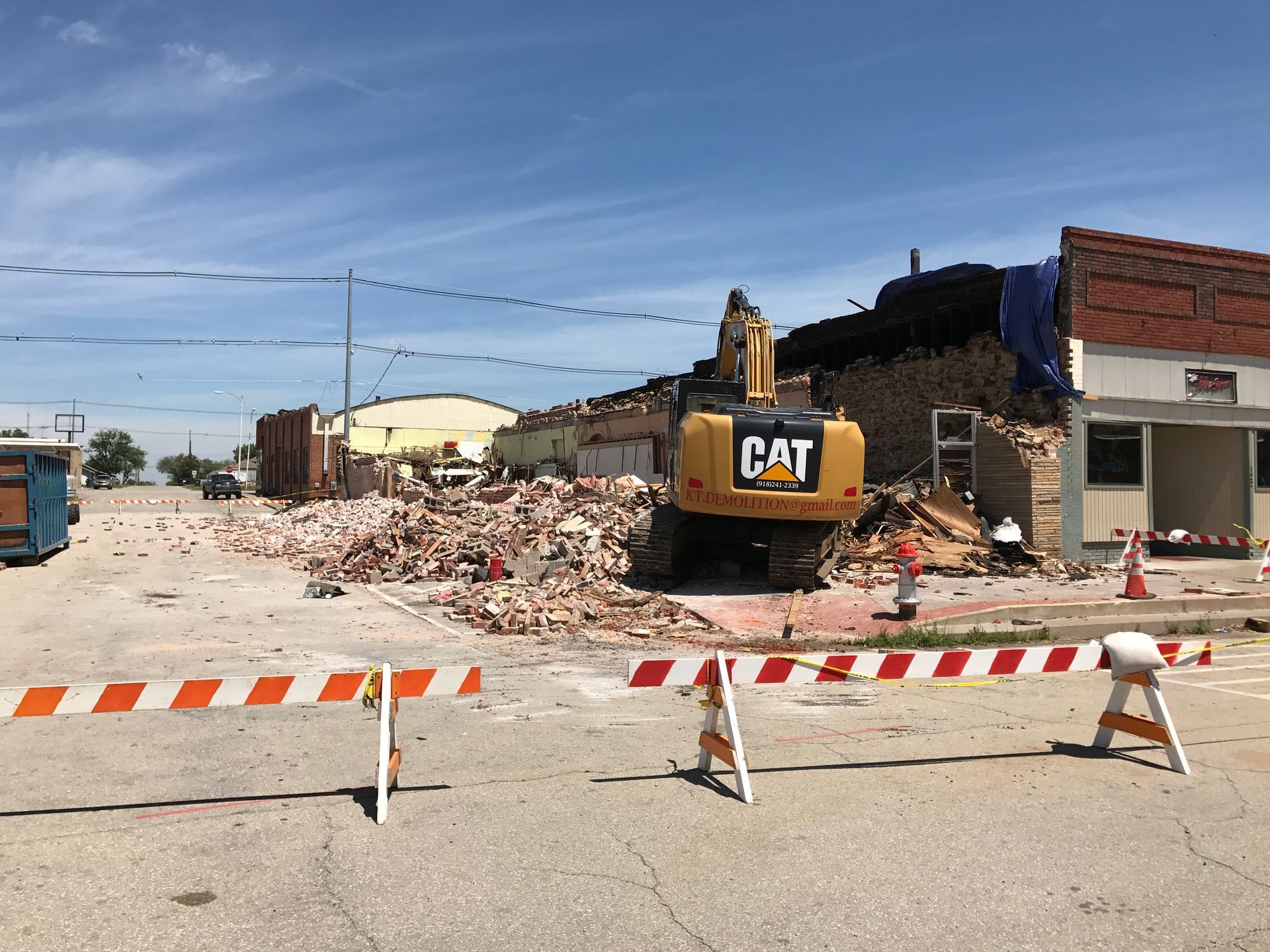 Demolition of a brick building by a Caterpillar excavator, with debris and road barricades.