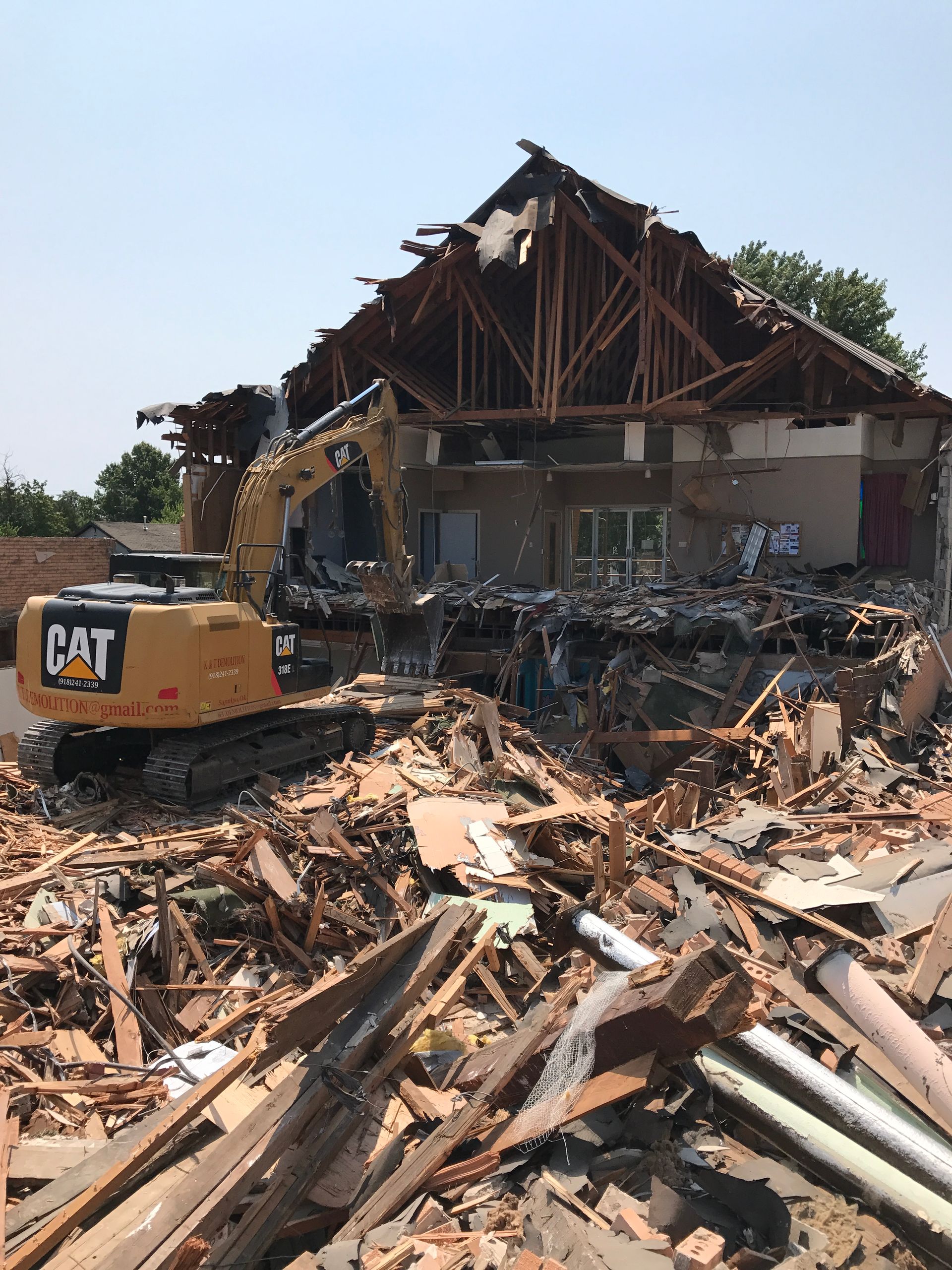 A yellow Caterpillar excavator demolishing a building on a sunny day; debris surrounds the site.